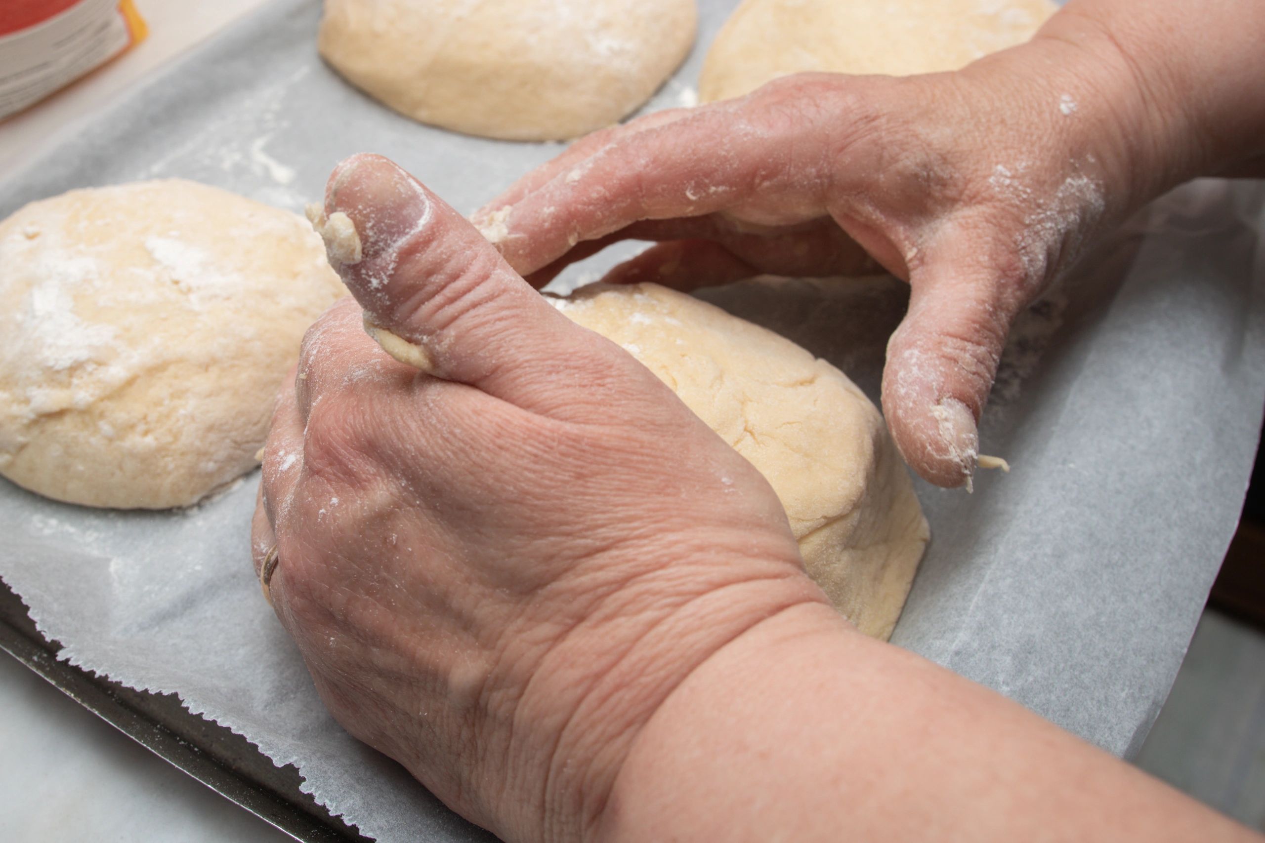 Hands shaping bread dough on a tray